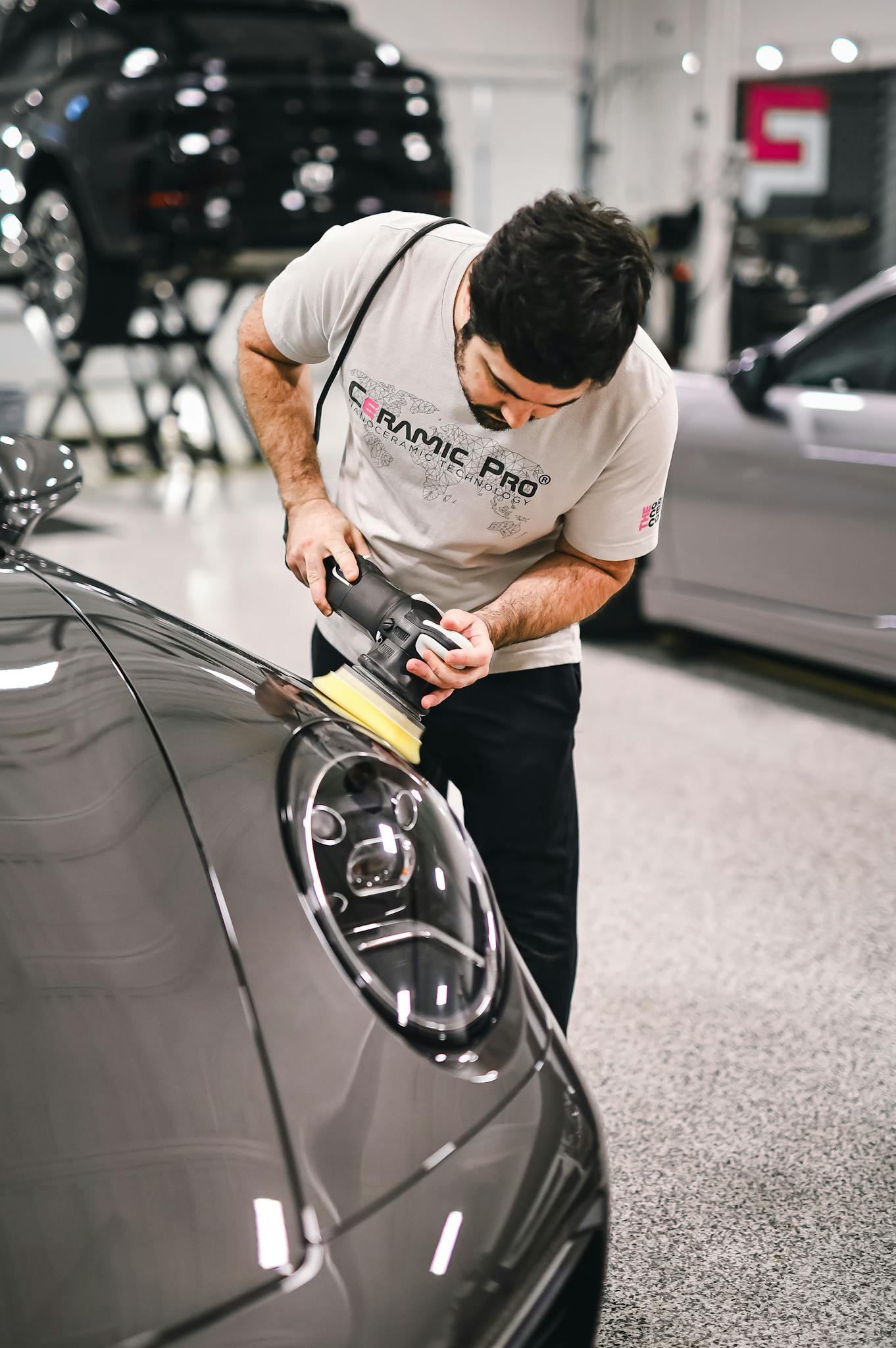 Man polishing a car's hood with precision in a modern automotive workshop.